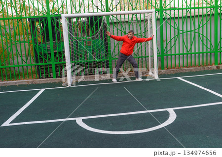 Active middle-aged man defending a soccer goal. Goalkeeper training on an outdoor sports field 134974656