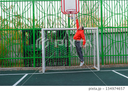 Man jumping to a basketball hoop on an outdoor court. Athlete playing inside a soccer goal Man jumping to a basketball hoop on an outdoor court. Athlete playing inside a soccer goal 134974657
