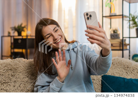 Smiling young woman blogger recording story on smartphone sitting on sofa in living room at home 134974838