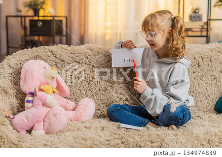 Young teenager girl pretending teacher at home sofa math lesson, toy students, playful serious act 134974839