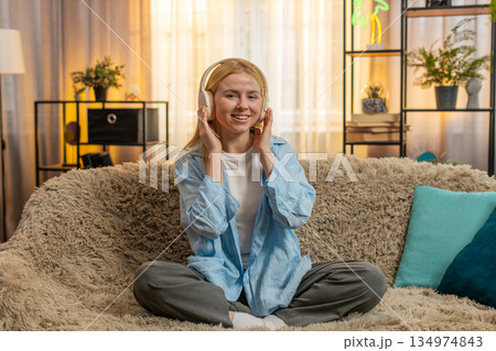 Young woman enjoying calm tunes at home, closed eyes, gentle sway, peaceful vibe, sofa relaxation 134974843