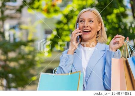 Happy mature businesswoman lady smiling laughs standing on city street holding shopping packages 134974881