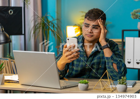 Sad Indian man use smartphone surprised by bad news fortune loss fail lottery online game results 134974903