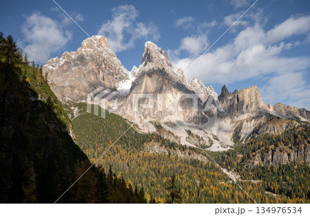 Dramatic rocky Dolomites mountain peaks above autumn forest under blue sky 134976534