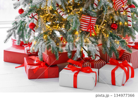Red wrapped gift boxes, presents under festive Christmas tree with lights and holiday decorations Red wrapped gift boxes, presents under festive Christmas tree with lights and holiday decorations 134977366