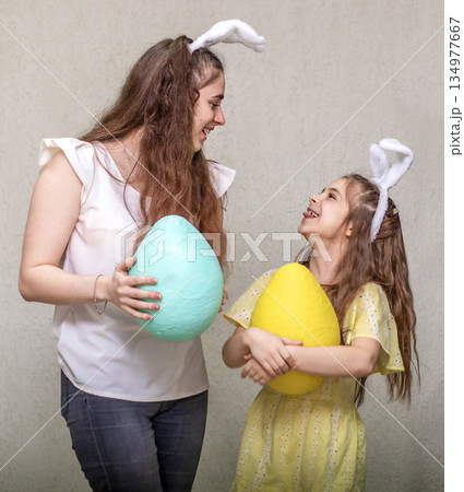 Mother and daughter holding colorful Easter eggs while smiling and celebrating together 134977667