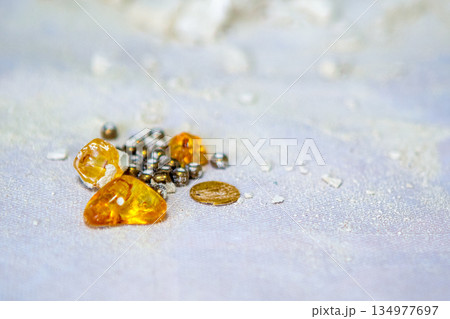 Amber Stones and Small Beads With a Coin on Pale Blue Fabric Background Amber Stones and Small Beads With a Coin on Pale Blue Fabric Background 134977697