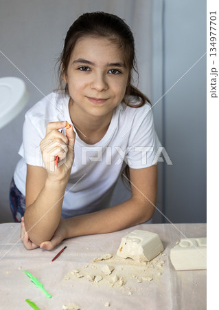 Young girl at a craft table shaping plaster with a tool during a creative project 134977701