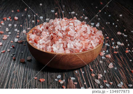 Wooden bowl filled with pink Himalayan salt crystals on dark wooden table, natural mineral seasoning for healthy cooking and spa concepts. 134977973