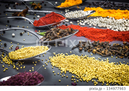 Collection of spices are spread out on a table. The spices include cumin, paprika, and turmeric 134977983