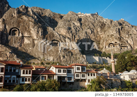 Ancient rock-cut tombs carved in cliff face above Amasya city with traditional Ottoman houses, mosque with minaret below in valley, heritage and historical architecture concept 134978005