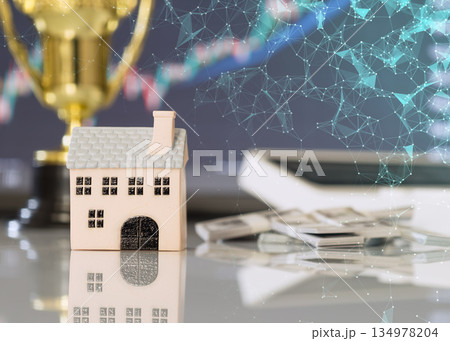 Miniature house with digital network overlay, cash, and financial chart, representing property investment, fintech, and real estate technology. 134978204