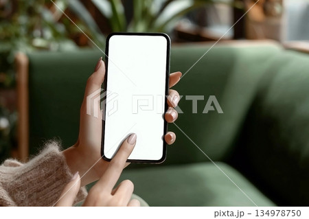 Close up of woman hand pointing on blank screen smartphone sitting on green sofa in cafe or lounge. Advertising Mockup, Social Media, Modern tech. 134978750