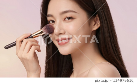 Beautiful young Asian woman applying blush with makeup brush in studio portrait Beautiful young Asian woman applying blush with makeup brush in studio portrait 134979616