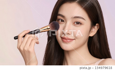Beautiful young Asian woman applying blush with makeup brush in studio portrait Beautiful young Asian woman applying blush with makeup brush in studio portrait 134979618