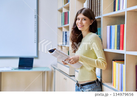 Portrait of teenage beautiful girl high school student with textbook in library classroom 134979656