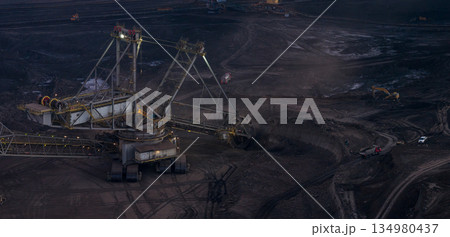 Ultra high resolution panoramic view of massive mining machines operating in an open pit coal mine, surrounded by dust and dramatic light. Powerful industrial scene showing large scale extraction, 134980437
