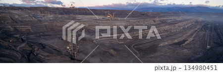 Ultra high resolution panoramic view of an open pit coal mine with massive mining machines, layered terrain, and dramatic sky on the horizon. Powerful industrial landscape showing large scale Ultra high resolution panoramic view of an open pit coal mine with massive mining machines, layered terrain, and dramatic sky on the horizon. Powerful industrial landscape showing large scale 134980451
