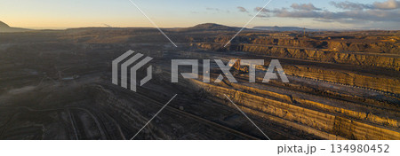 Ultra high resolution panoramic view of an open pit coal mine with massive mining machines, layered terrain, and dramatic sky on the horizon. Powerful industrial landscape showing large scale 134980452