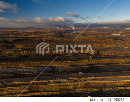 Ultra high resolution panoramic view of an open pit coal mine with massive mining machines, layered terrain, and dramatic sky on the horizon. Powerful industrial landscape showing large scale 134980454