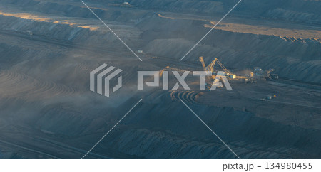 High resolution panoramic view of massive mining machines in an open pit coal mine, surrounded by dust. Powerful industrial scene showing large scale extraction, energy production, and human impact. 134980455