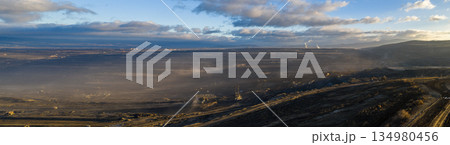 Ultra high resolution panoramic view of an open pit coal mine with massive mining machines, layered terrain, and dramatic sky on the horizon. Powerful industrial landscape showing large scale Ultra high resolution panoramic view of an open pit coal mine with massive mining machines, layered terrain, and dramatic sky on the horizon. Powerful industrial landscape showing large scale 134980456