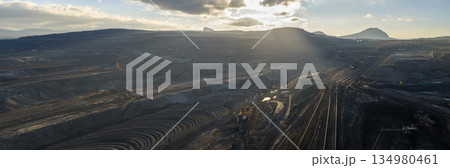 Ultra high resolution panoramic view of an open pit coal mine with massive mining machines, layered terrain, and dramatic sky on the horizon. Powerful industrial landscape showing large scale Ultra high resolution panoramic view of an open pit coal mine with massive mining machines, layered terrain, and dramatic sky on the horizon. Powerful industrial landscape showing large scale 134980461