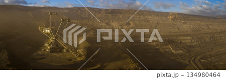Ultra high resolution panoramic view of an open pit coal mine with massive mining machines, layered terrain, and dramatic sky on the horizon. Powerful industrial landscape showing large scale 134980464