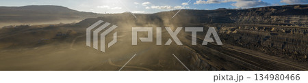 Ultra high resolution panoramic view of an open pit coal mine with massive mining machines, layered terrain, and dramatic sky on the horizon. Powerful industrial landscape showing large scale Ultra high resolution panoramic view of an open pit coal mine with massive mining machines, layered terrain, and dramatic sky on the horizon. Powerful industrial landscape showing large scale 134980466