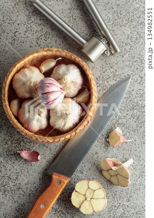 Garlic, knife, and garlic press on a kitchen table. Garlic, knife, and garlic press on a kitchen table. 134982551