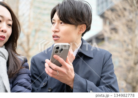 オフィス街でスマホを使用する男女 オフィス街でスマホを使用する男女 134982778