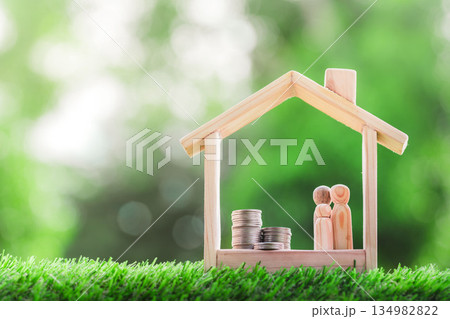 Wooden house with a pile of money and wooden dolls a happy family is placed inside on nature bokeh. Wooden house with a pile of money and wooden dolls a happy family is placed inside on nature bokeh. 134982822