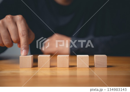 Closeup of a man hand making a pose and sign gesture by pointing to the first wooden cube, a conceptual sign for starting a new business plan or creative idea. 134983143