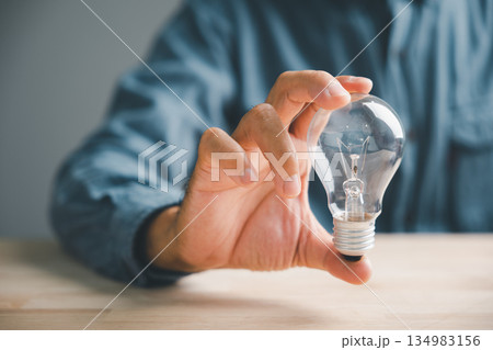 A closeup man hand pose and gesture holding a lightbulb is a creative sign of inspiration, a hopeful sign representing a brilliant new idea for business or technology. A closeup man hand pose and gesture holding a lightbulb is a creative sign of inspiration, a hopeful sign representing a brilliant new idea for business or technology. 134983156