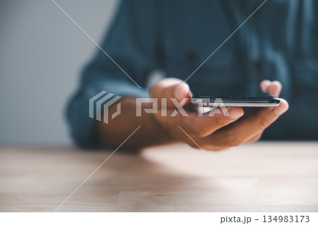 Close-up of hand holding a smartphone with a blurred background. The hand is resting on a wooden surface. 134983173
