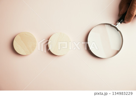 Two wooden circles and a magnifying glass on a pale pink background. Two wooden circles and a magnifying glass on a pale pink background. 134983229