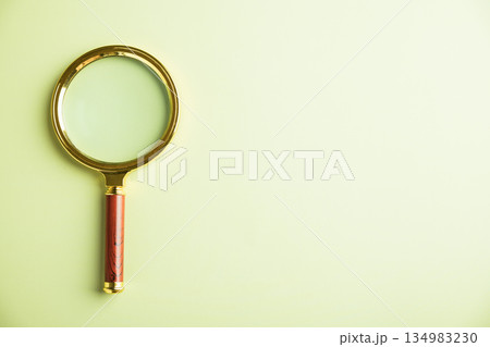 Golden magnifying glass with a wooden handle on a light green background. . Golden magnifying glass with a wooden handle on a light green background. . 134983230
