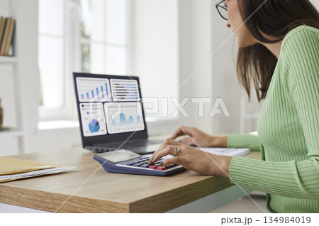 Female accountant analyzing charts on laptop with calculator for audit work 134984019