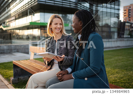 Two diverse businesswomen discussing corporate strategy using digital tablet Two diverse businesswomen discussing corporate strategy using digital tablet 134984965