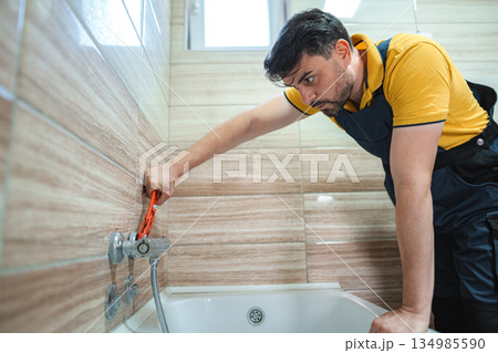 Plumber tightening faucet in bathroom using pipe wrench Plumber tightening faucet in bathroom using pipe wrench 134985590