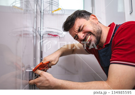 Plumber struggling while tightening a plumbing fitting in a bathroom Plumber struggling while tightening a plumbing fitting in a bathroom 134985595
