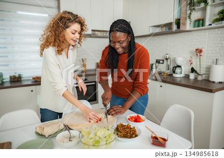 Diverse women cooking healthy food together in kitchen Diverse women cooking healthy food together in kitchen 134985618