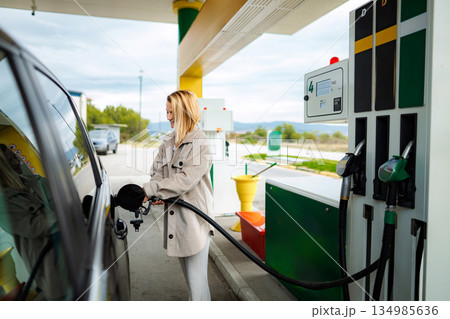 Woman refueling car at gas station, filling up tank 134985636