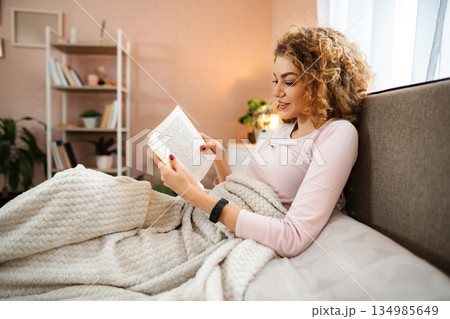 Young woman enjoying leisure time reading book in bed 134985649