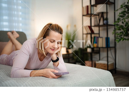 Young woman relaxing on bed using smartphone at home 134985737