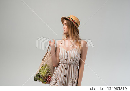 Young woman holding reusable mesh shopping bag with vegetables and bread, sustainable grocery shopping concept, healthy food lifestyle Young woman holding reusable mesh shopping bag with vegetables and bread, sustainable grocery shopping concept, healthy food lifestyle 134985819