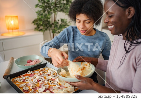 Mother and daughter making homemade pizza getting ready to bake Mother and daughter making homemade pizza getting ready to bake 134985828