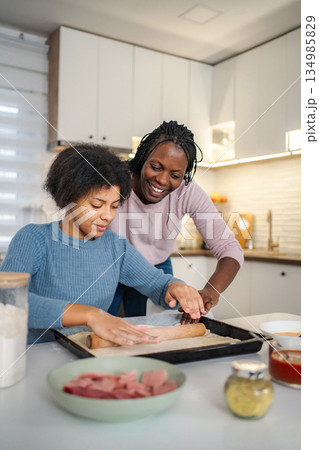 Mother and daughter rolling dough in kitchen, bonding while baking Mother and daughter rolling dough in kitchen, bonding while baking 134985829