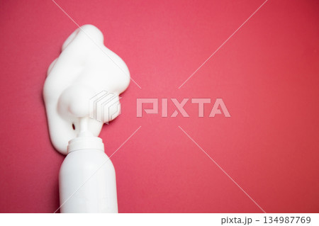 Close-up view from above in the center of a bottle of foam for long-lasting hair styling lies on a pink background with space for text, white foam has spilled out of it. The concept of styling, fixing 134987769