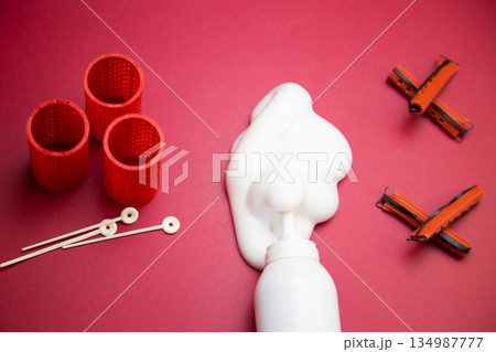 Close-up view from above in the center of a bottle of foam for long-lasting hair styling lies on a pink background, white foam has poured out of it, next to it are round curlers for large curls and Close-up view from above in the center of a bottle of foam for long-lasting hair styling lies on a pink background, white foam has poured out of it, next to it are round curlers for large curls and 134987777